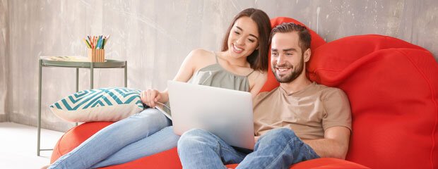 couple sitting on a red couch looking for hotel deals online using their computer 